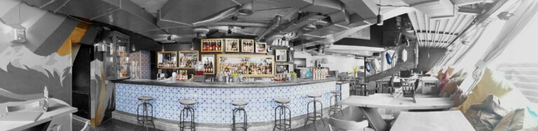 Bar area of Wohnzimmer Bar in Innsbruck, Austria, featuring a sleek, illuminated counter with mosaic tiles, high stools, and a well-stocked selection of spirits, creating a stylish and inviting atmosphere for cocktail enthusiasts Bar area of Wohnzimmer Bar in Innsbruck, Austria, featuring a sleek, illuminated counter with mosaic tiles, high stools, and a well-stocked selection of spirits, creating a stylish and inviting atmosphere for cocktail enthusiasts